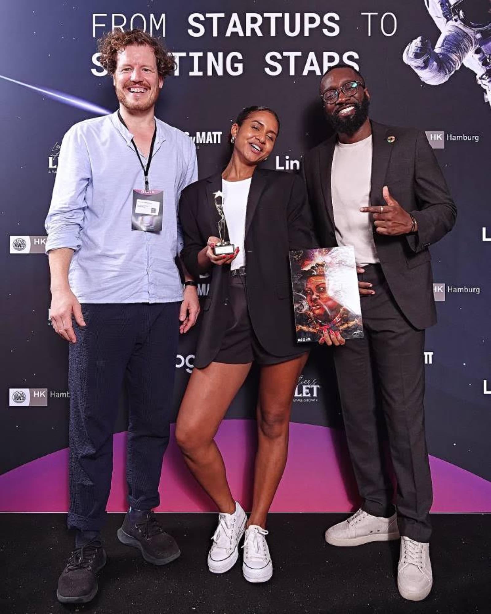 Dr. Simon Springmann mit Madeleine und Jeff bei der AIDIA-Auszeichnung „From Startups to Starting Stars" in der Handelskammer Hamburg, die Pitch-Gewinnerin hält Trophäe und Plakat