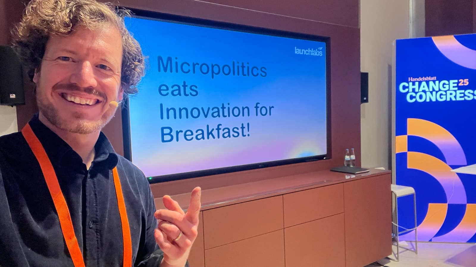 Dr. Simon Springmann mit Headset-Mikrofon vor seiner Keynote-Slide „Micropolitics eats Innovation for Breakfast!" beim Handelsblatt Change Congress 2025 in Berlin