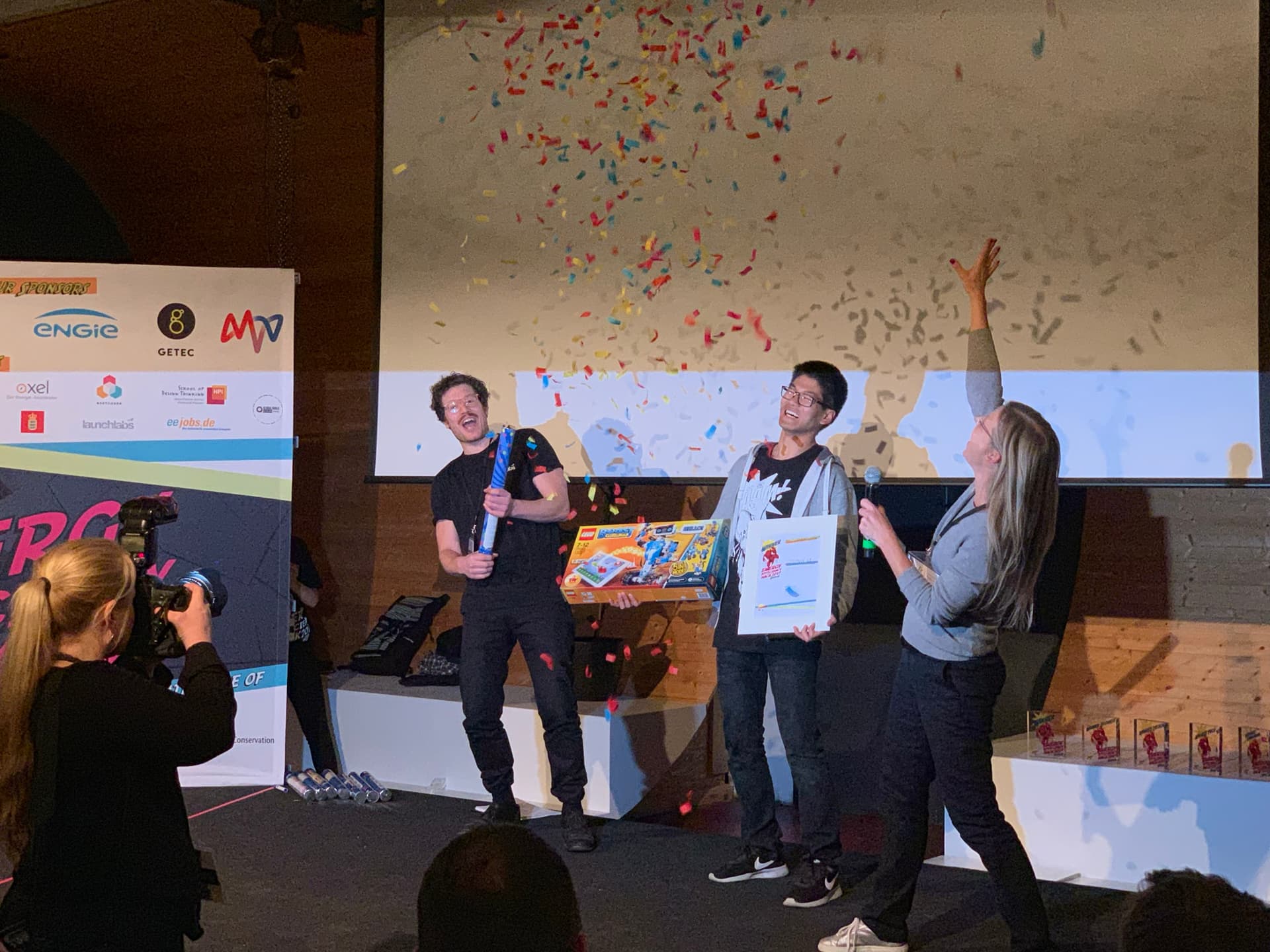 Preisverleihung beim DENEFF Energy Efficiency Hack 2019 mit Konfetti, Dr. Simon Springmann (l.) als Jurymitglied gratuliert den Gewinnern