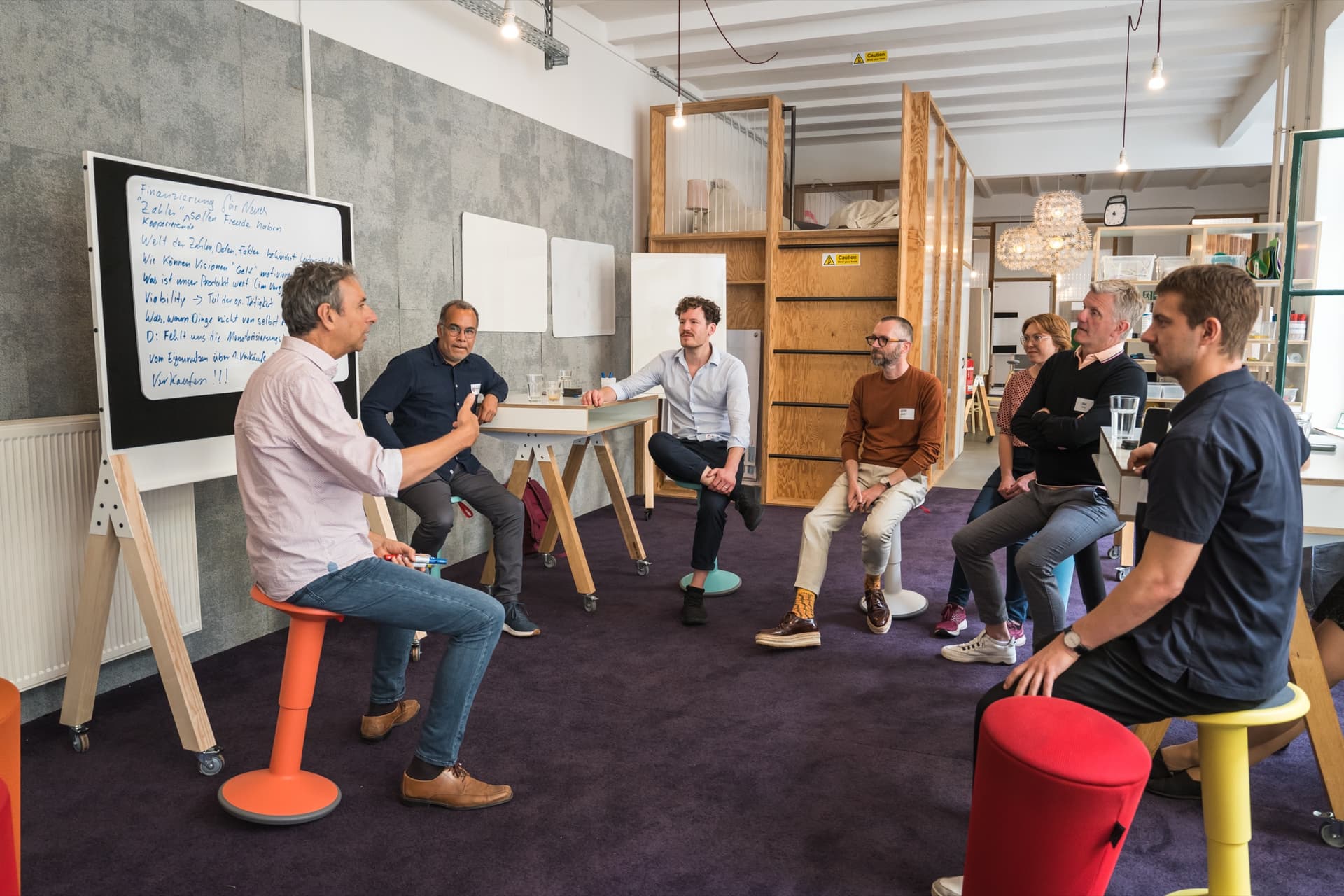 Dr. Simon Springmann in einer Working Session beim LaunchX-Event 2023 in Berlin im Gespräch mit Gründer:innen, im Hintergrund ein Whiteboard mit Notizen zu Finanzierung, Vision und Geschäftsmodell