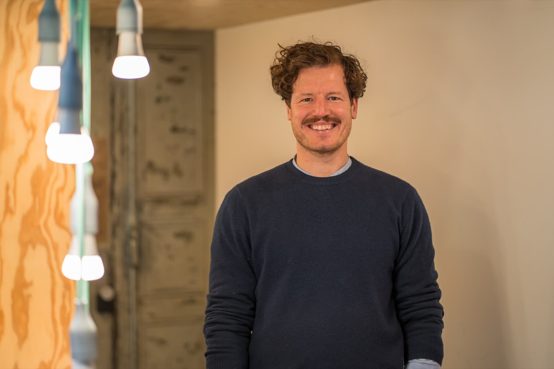 Dr. Simon Springmann, Managing Partner at launchlabs, smiling in a wood-and-concrete studio with hanging pendant lights